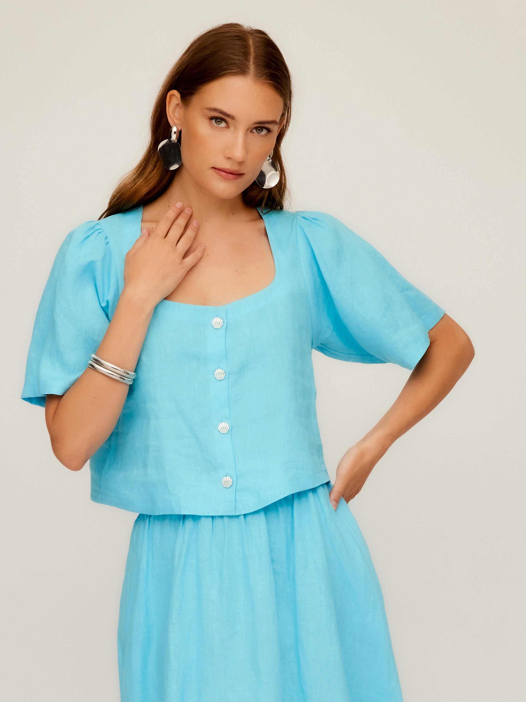 Woman wearing light blue Pia Poof Sleeve Linen Top with square neck, short puff sleeves, and button front closure.