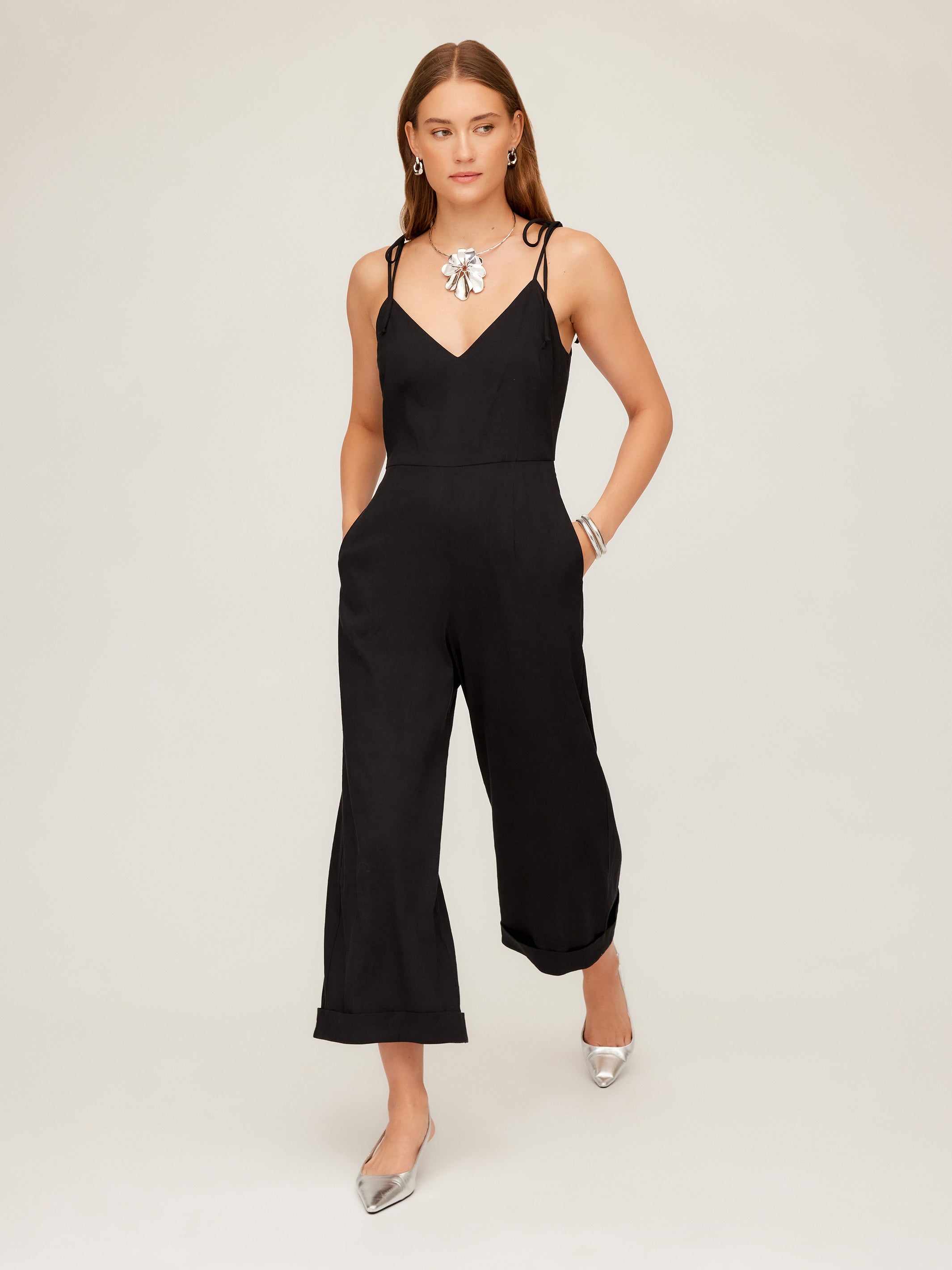 Woman wearing a black Dana Cropped Jumpsuit with wide cropped legs, adjustable tie straps, and side pockets.