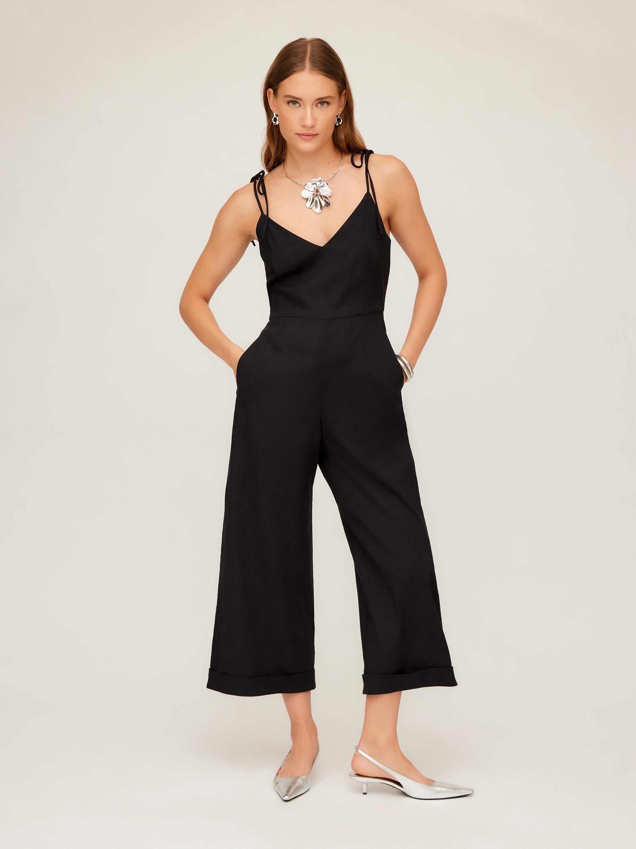 Woman wearing black Dana Cropped Jumpsuit with cropped wide leg and cuffed hem, styled with silver flats and statement necklace