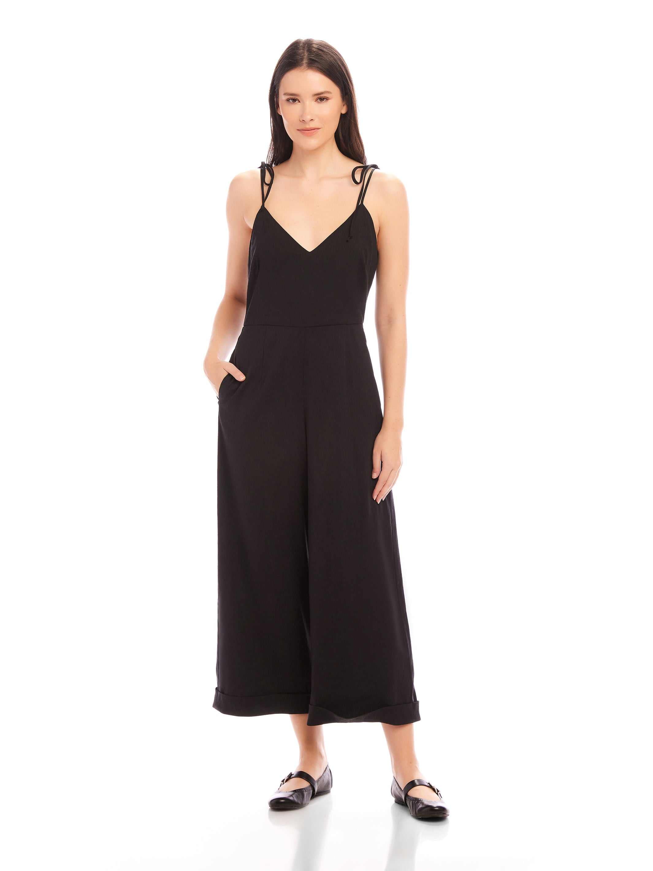 Woman wearing black Dana Cropped Jumpsuit with V-neck, adjustable tie straps, and cropped wide legs.