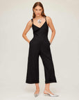 Woman wearing black Dana Cropped Jumpsuit with cropped wide leg and cuffed hem, styled with silver flats and statement necklace