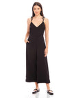 Woman wearing black Dana Cropped Jumpsuit with V-neck, adjustable tie straps, and cropped wide legs.