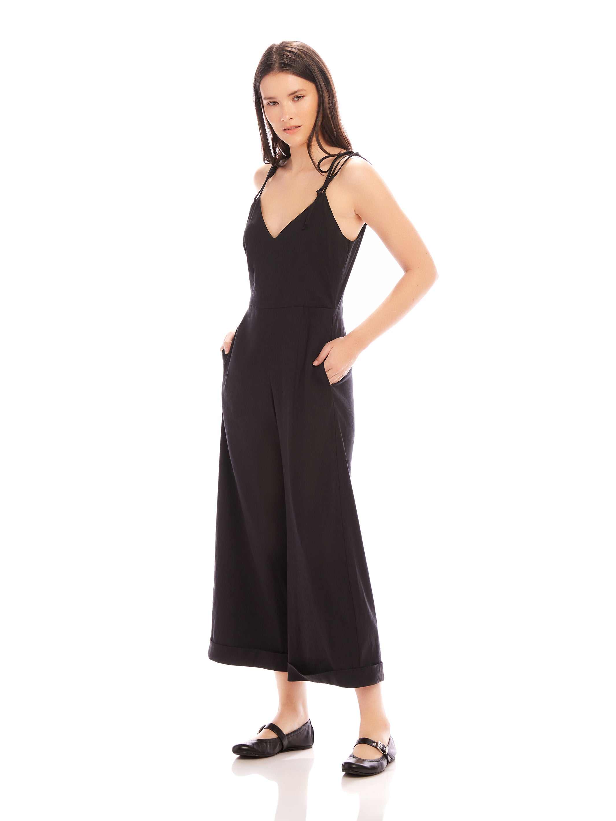 Woman wearing black Dana Cropped Jumpsuit with V-neck and cropped wide legs, styled with flat shoes