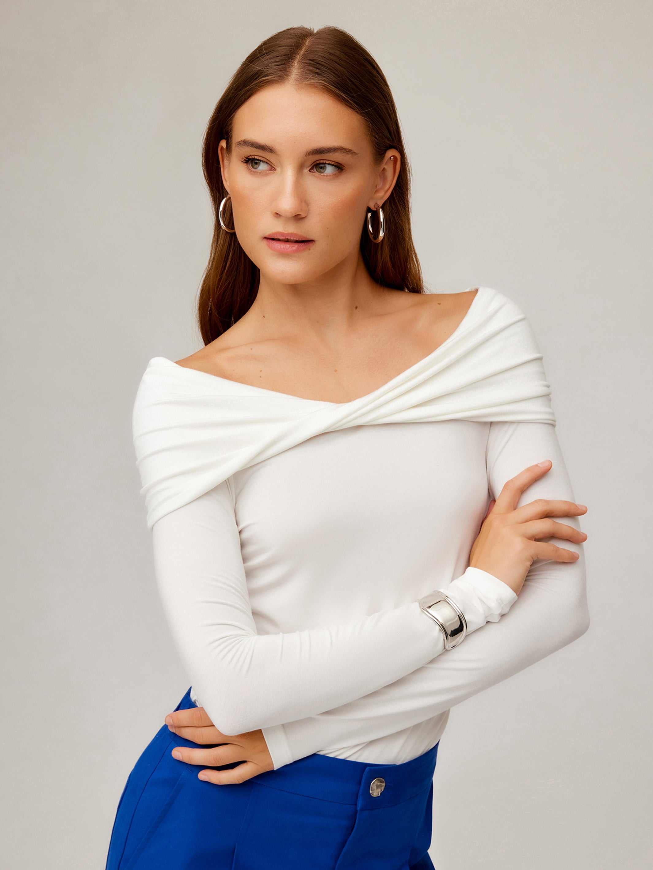 Woman wearing a white long sleeve off-the-shoulder top with a twisted front and side shirring detail.