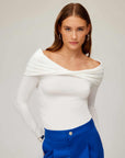 Woman wearing a white fitted off-the-shoulder top with twist front and side shirring detail paired with blue pants