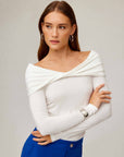 Woman wearing a white long sleeve off-the-shoulder top with a twisted front and side shirring detail.