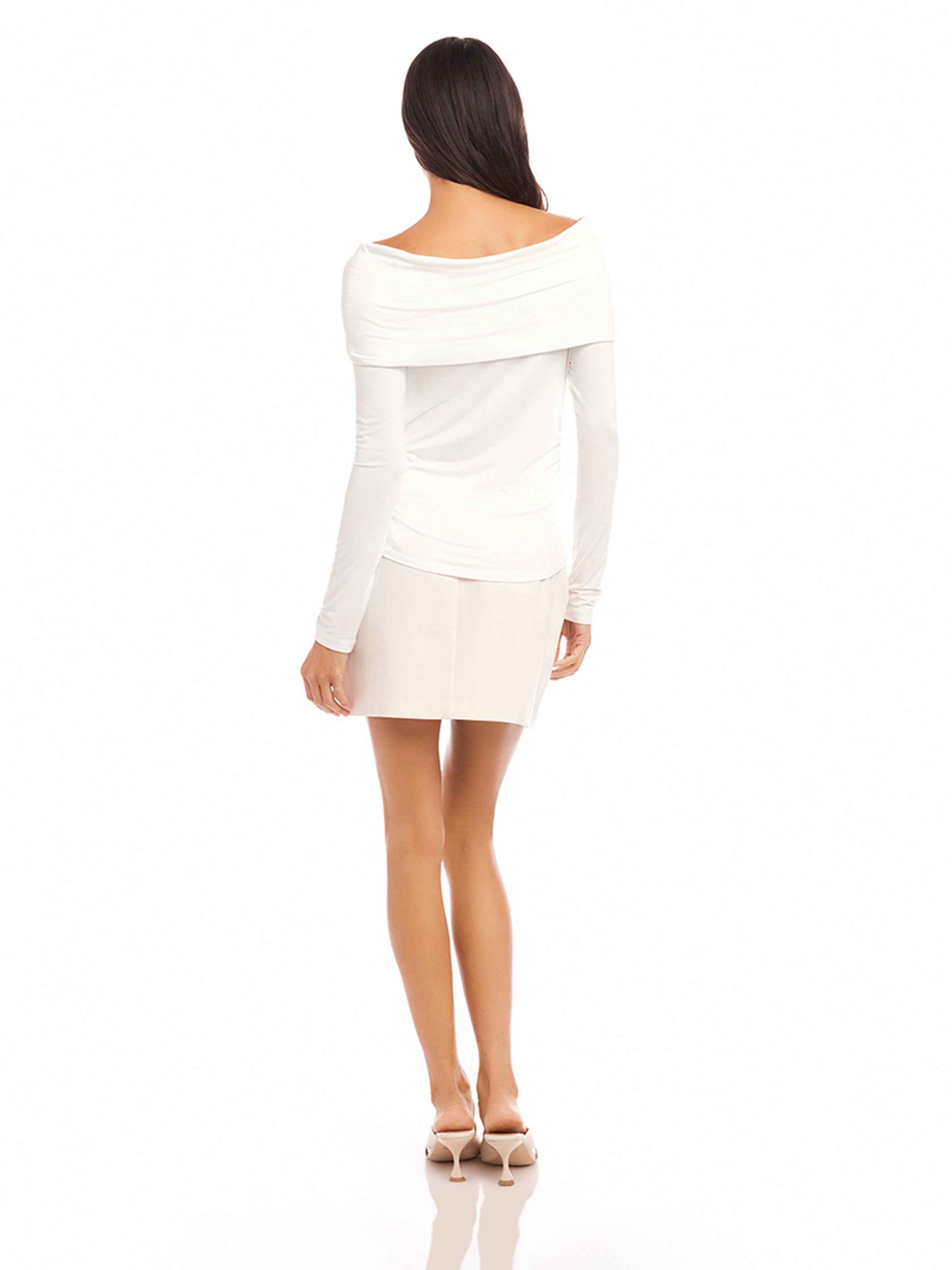Woman wearing white Jillian off-the-shoulder top with twist front and long sleeves.