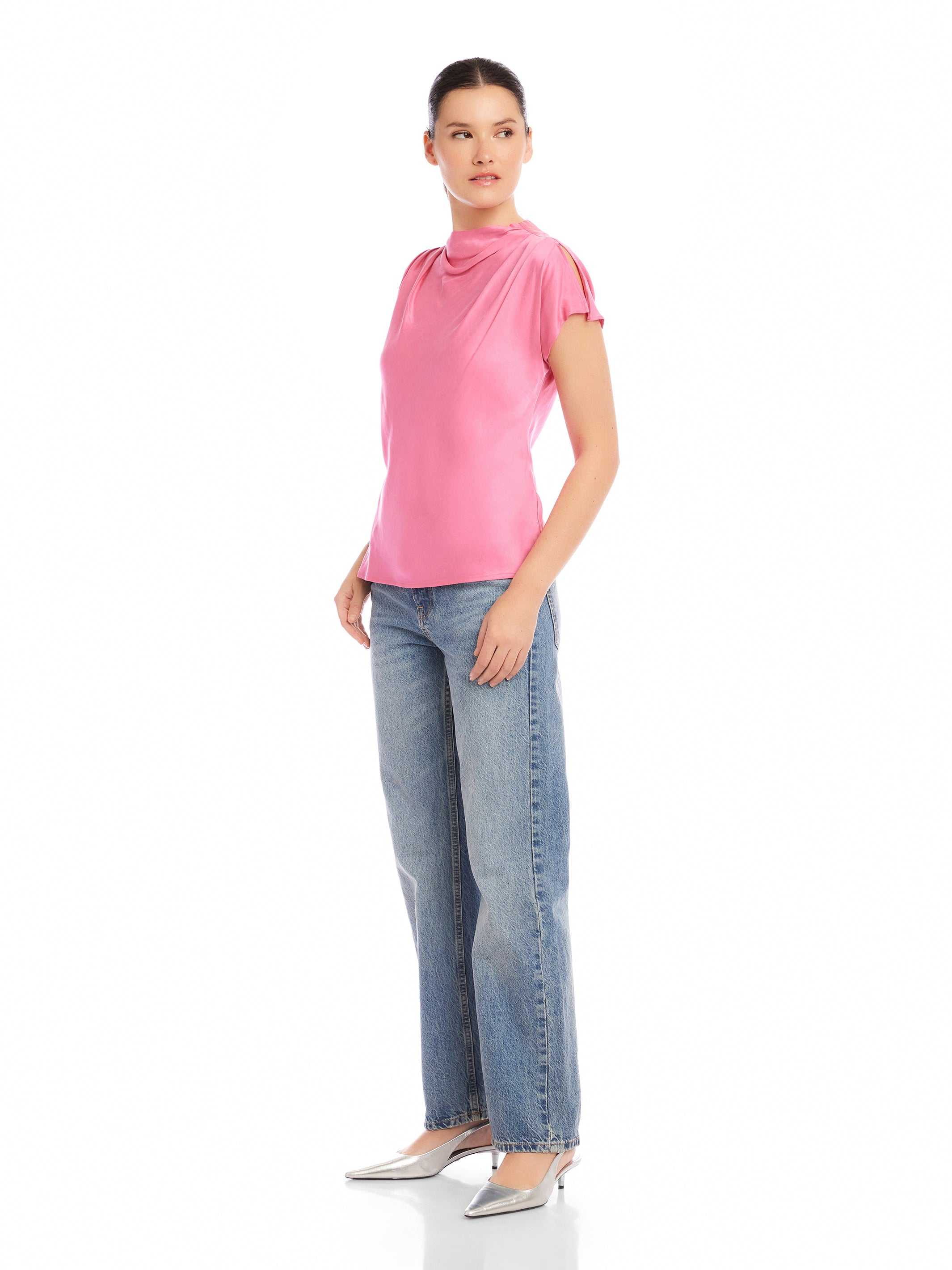 Woman wearing pink Emmeline blouse made of silky cupro material with mock cowl neck and split cap sleeves paired with blue jeans and silver heels