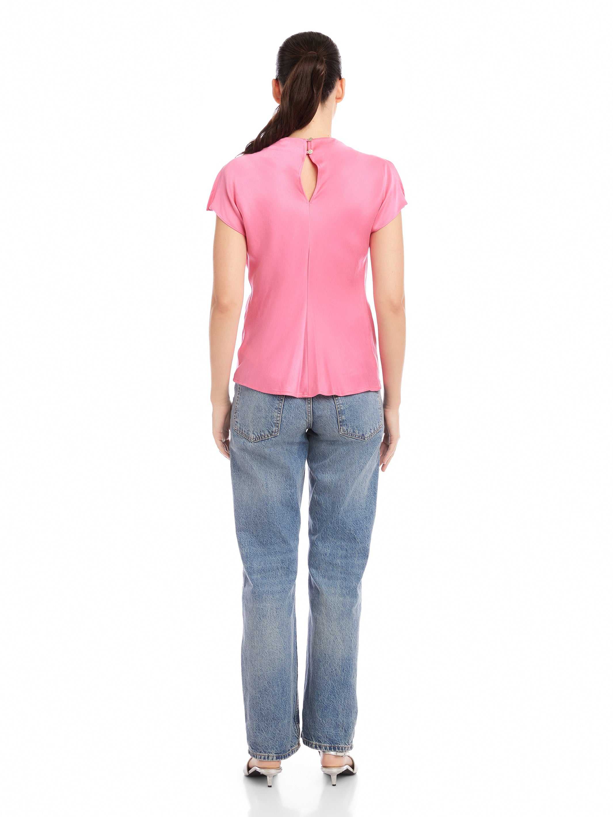 Back view of woman wearing pink Emmeline blouse made from silky cupro material with split cap sleeves and keyhole closure paired with blue jeans