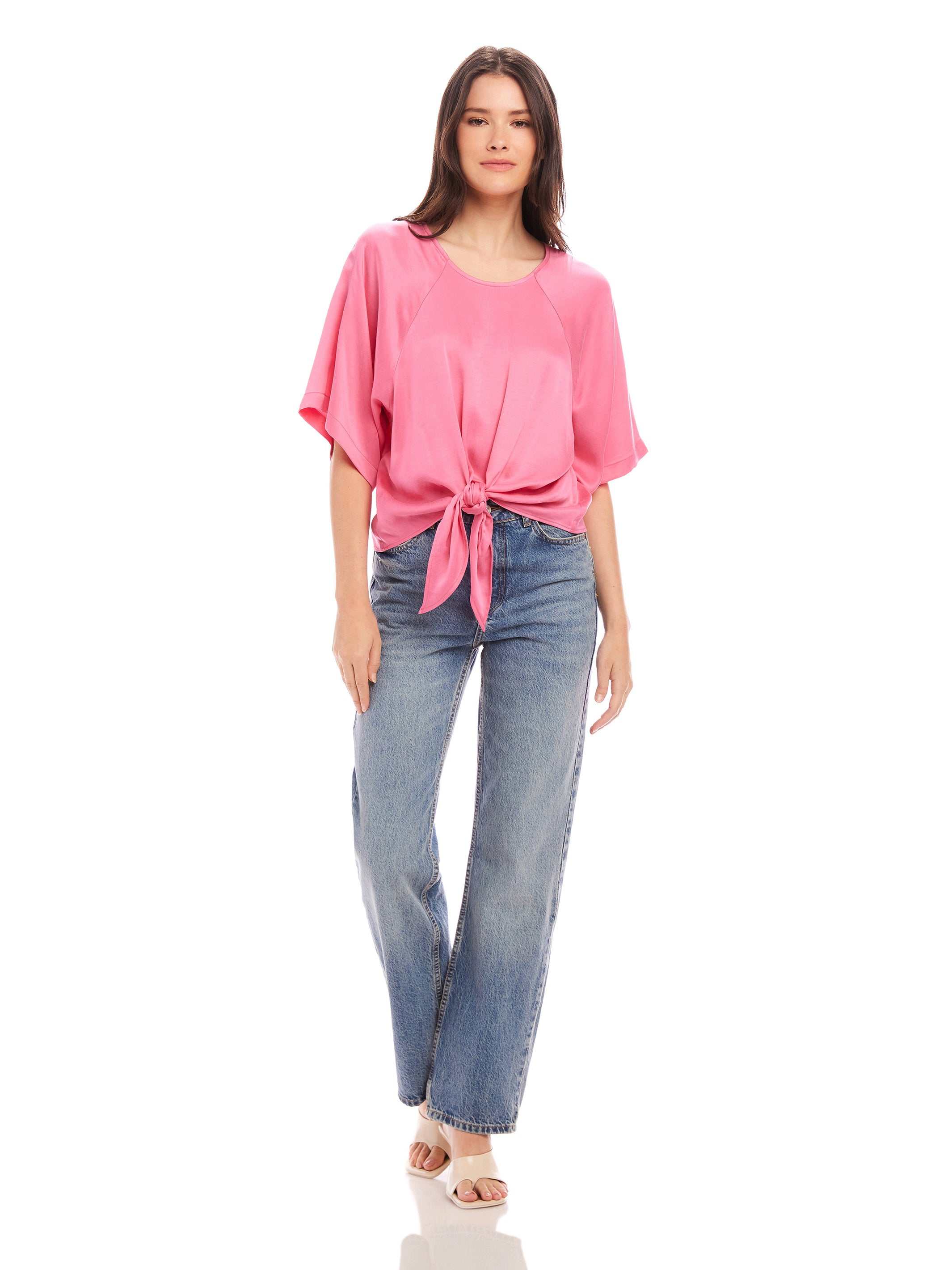 Woman wearing pink Seline Tie-Front Top with high waist jeans and sandals against a white background