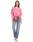 Woman wearing pink Seline Tie-Front Top with high waist jeans and sandals against a white background