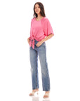 Woman wearing pink Seline Tie-Front Top with dolman sleeves and blue high waist jeans