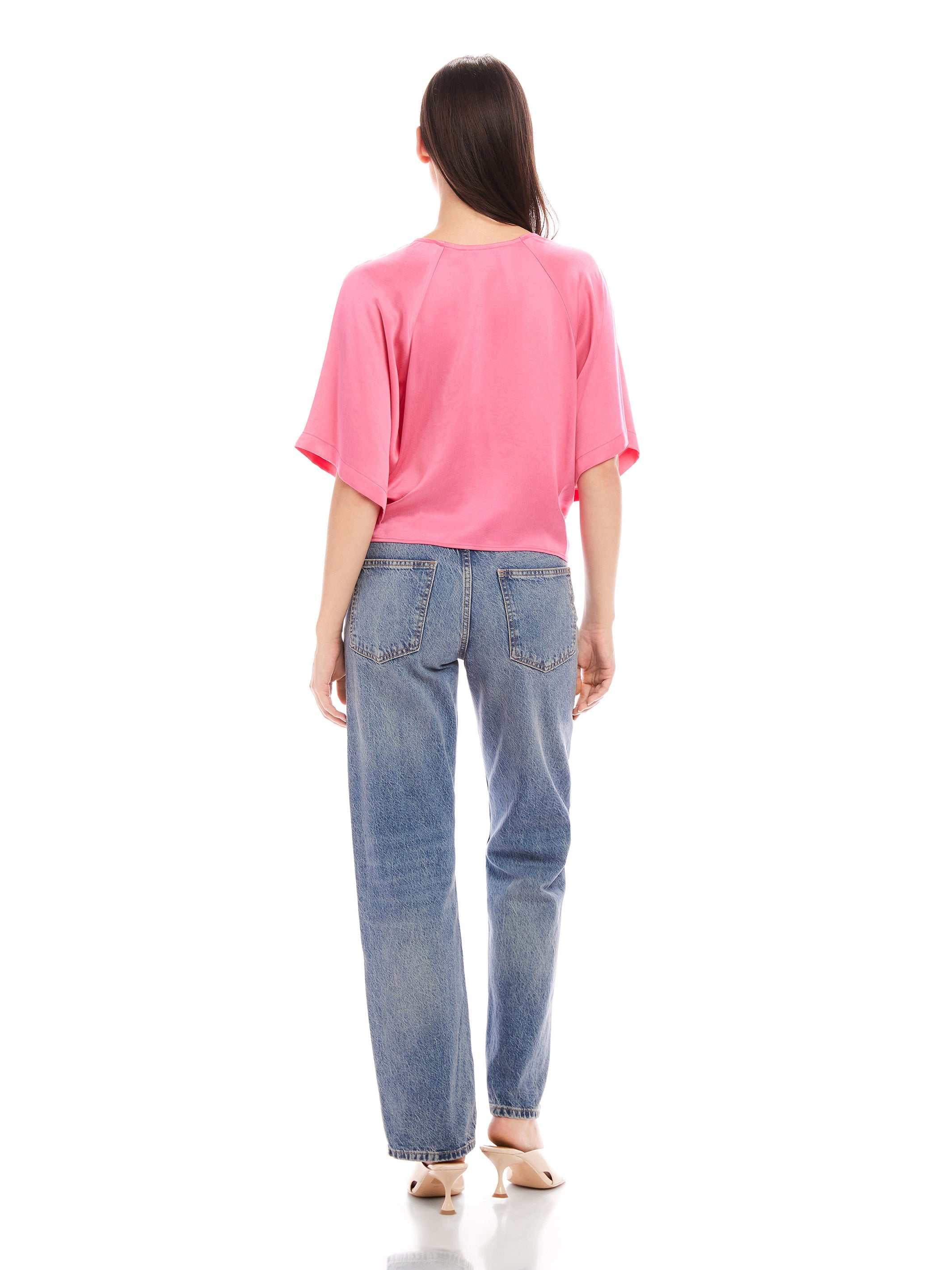 Woman wearing pink Seline Tie-Front Top with dolman sleeves and blue high-waist jeans, back view