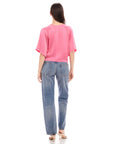 Woman wearing pink Seline Tie-Front Top with dolman sleeves and blue high-waist jeans, back view