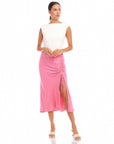 Woman wearing a pink Fiona Shirred Midi Skirt with side shirring and high slit, paired with a white sleeveless top and open-toe heels.