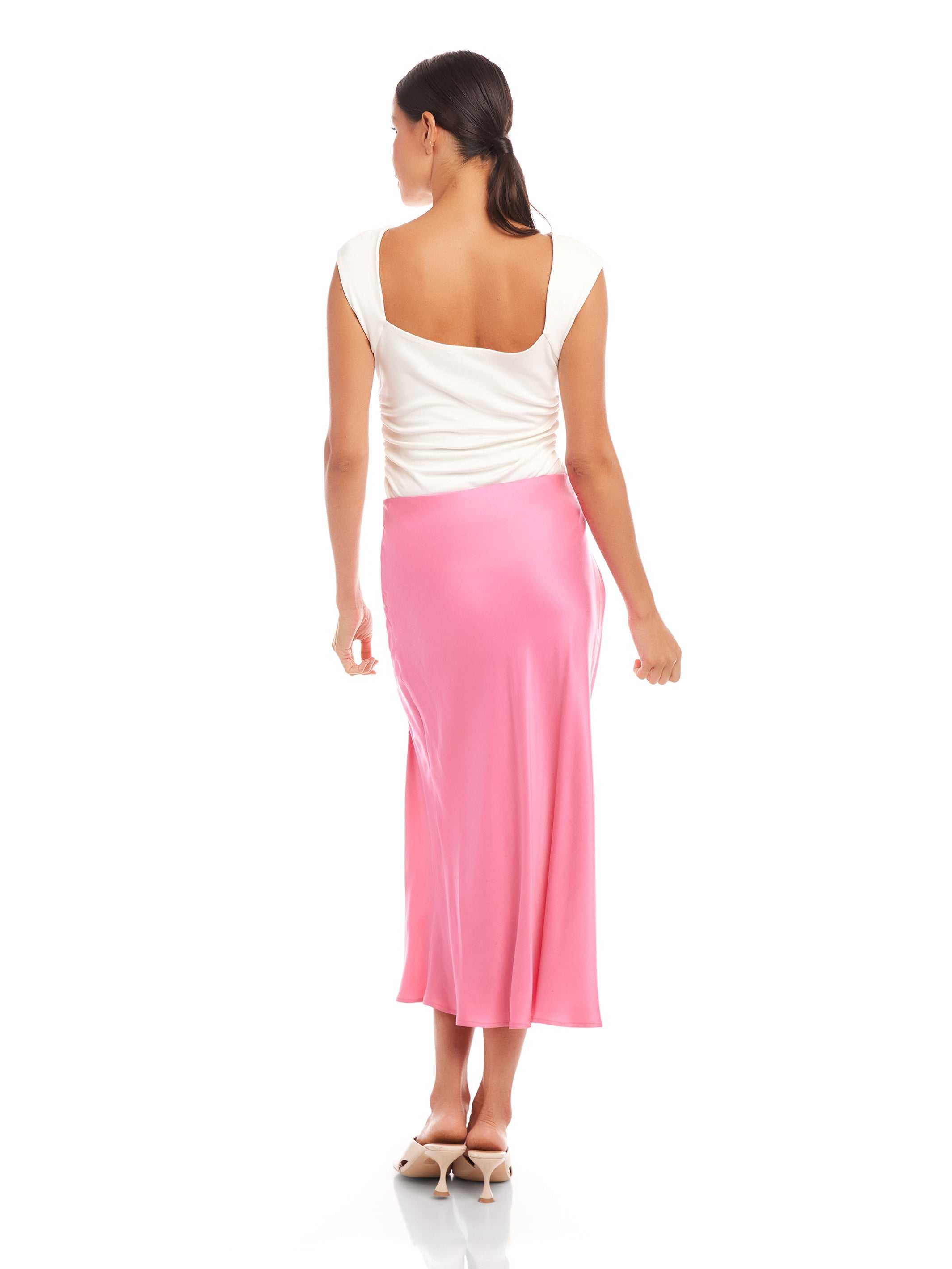 Woman wearing a pink Fiona Shirred Midi Skirt with side shirring and high slit, paired with a white sleeveless top, viewed from the back.