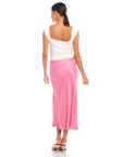 Woman wearing a pink Fiona Shirred Midi Skirt with side shirring and high slit, paired with a white sleeveless top, viewed from the back.