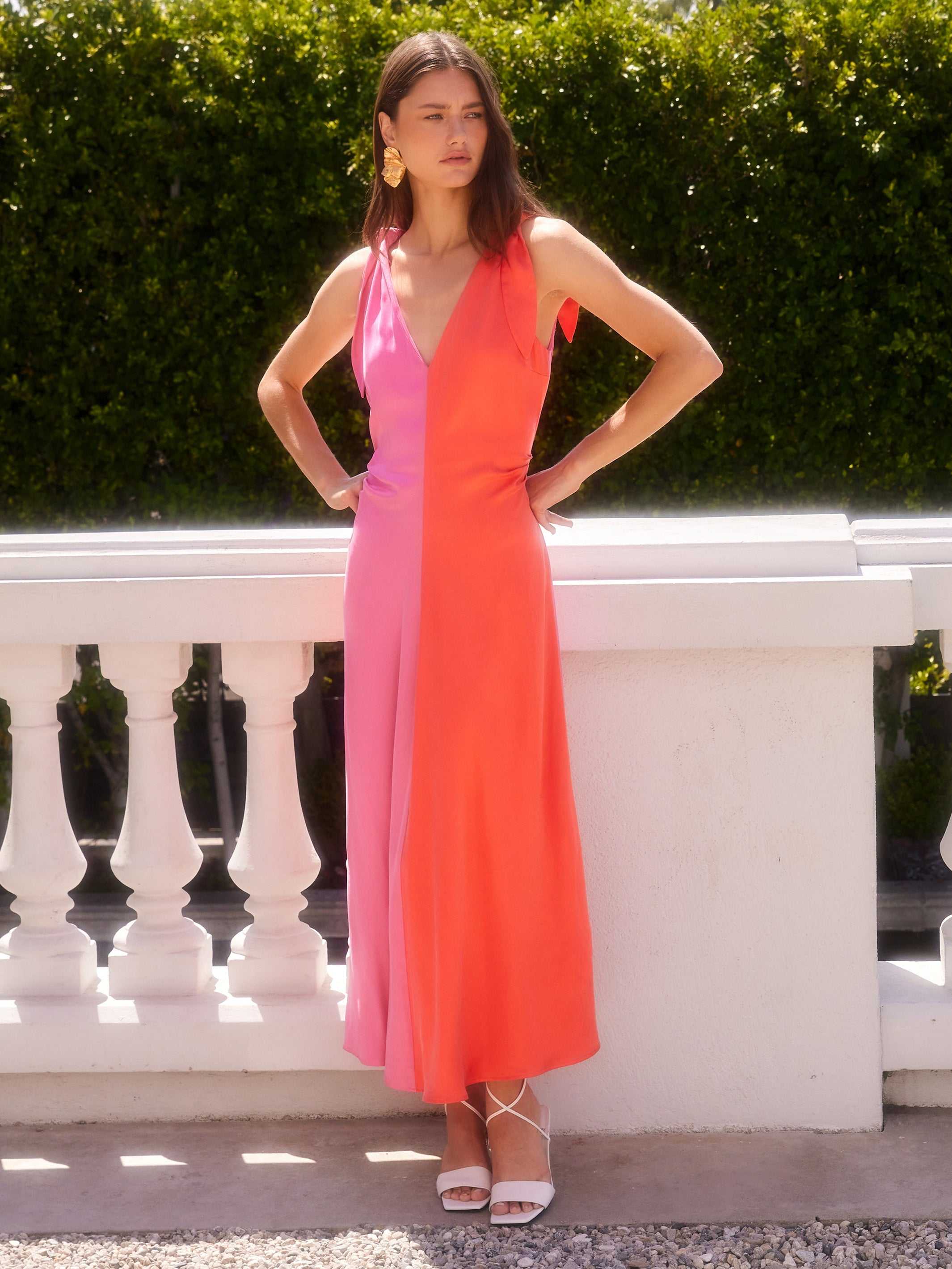 Woman wearing Verity Two-Tone Midi Dress in coral and pink with pleated A-line silhouette and low V-neck standing outdoors