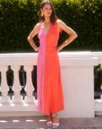 Woman wearing Verity Two-Tone Midi Dress in coral and pink with pleated A-line silhouette and low V-neck standing outdoors