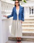 Woman wearing a Chelsea Cropped Trench denim jacket with double breast buttons and notch collar over a white striped dress