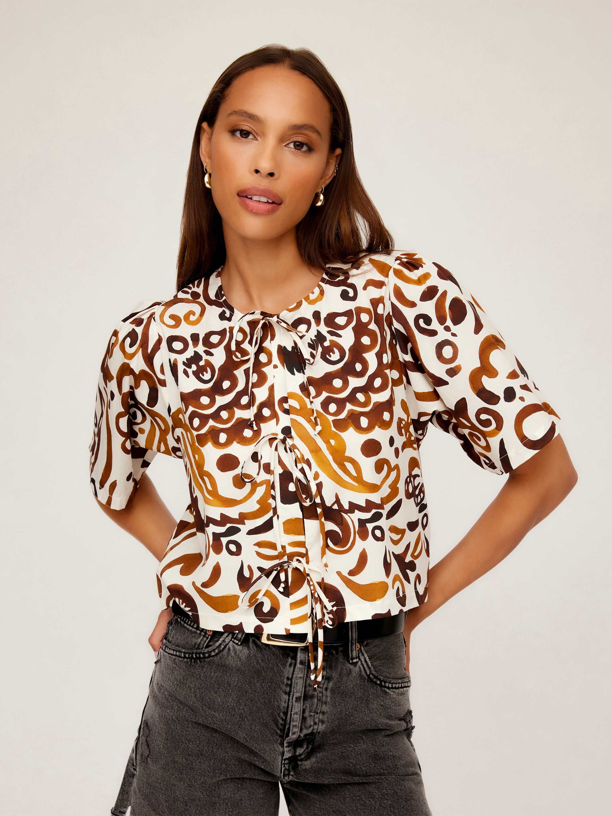 Nadine Bow Detail Top with brown and white stamped batik print, short puff sleeves, front tie closure, and semi-cropped boxy fit modeled with high waist jeans