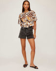 Woman wearing Nadine Bow Detail Top with front tie closure and puff sleeves paired with black denim shorts and slip-on sandals