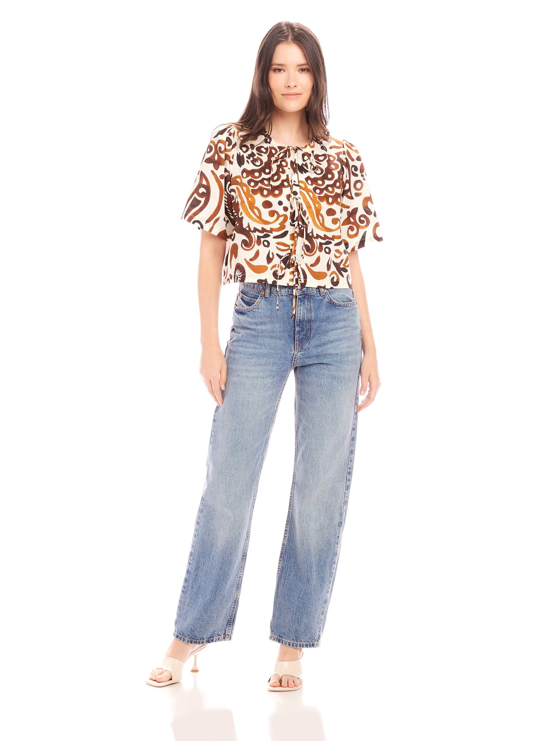 Woman wearing Nadine Bow Detail Top with front tie and short puff sleeves paired with high waist jeans