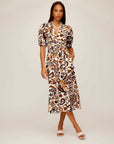 Woman wearing a Poppy Shirred Waist Dress with paisley print, V-neckline, short puff sleeves, elasticized fitted waist, and mid-thigh side slit.