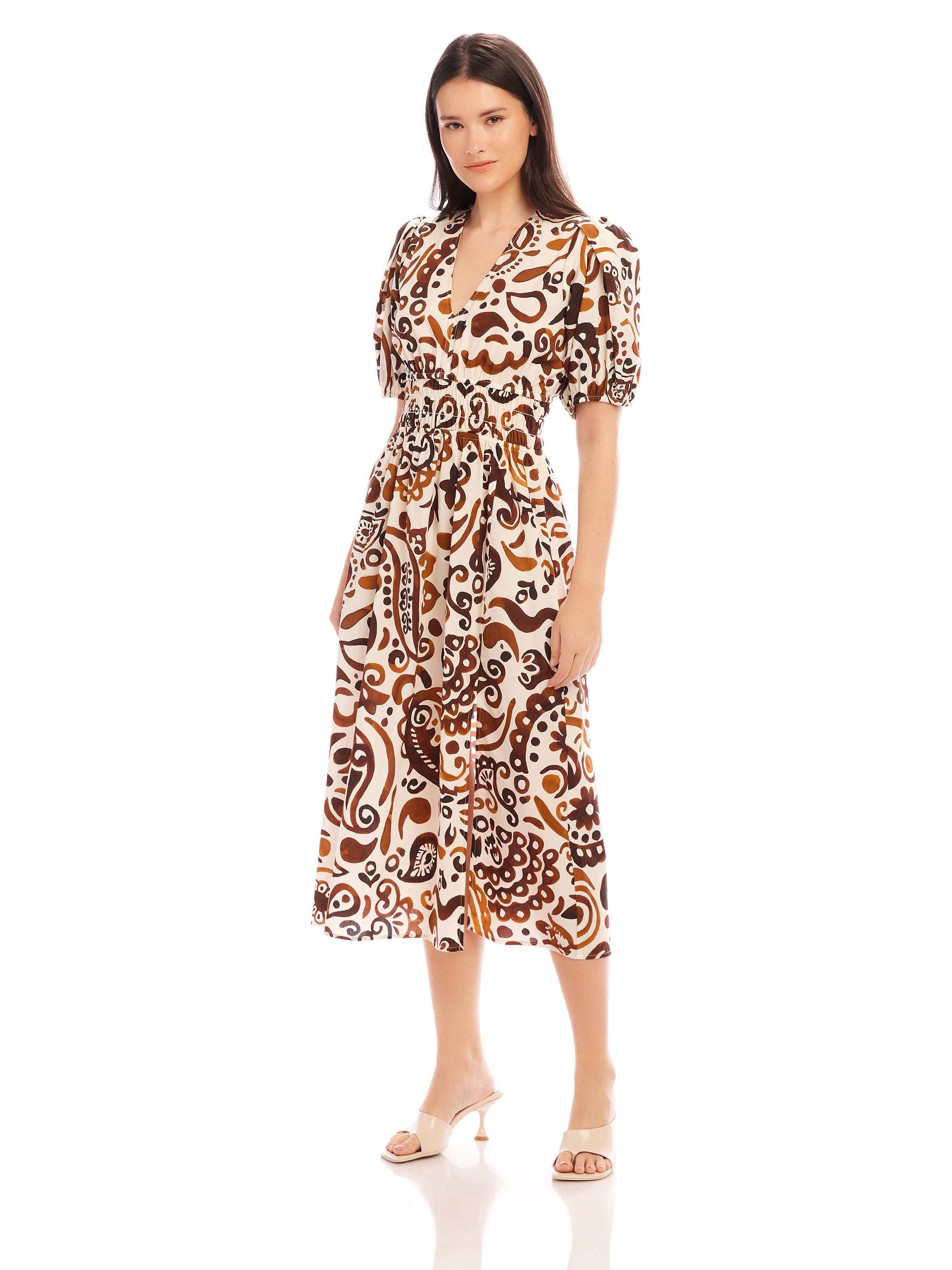 Woman wearing a brown and white paisley print Poppy Shirred Waist Dress with puff sleeves and side slit