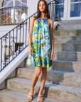 woman wearing sleeveless Brenda ruffle hem dress with botanical floral print and halter neckline standing on outdoor stairs