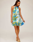 Woman wearing sleeveless halter neckline Brenda Ruffle Hem Dress with botanical floral scarf print and blue-green tones.