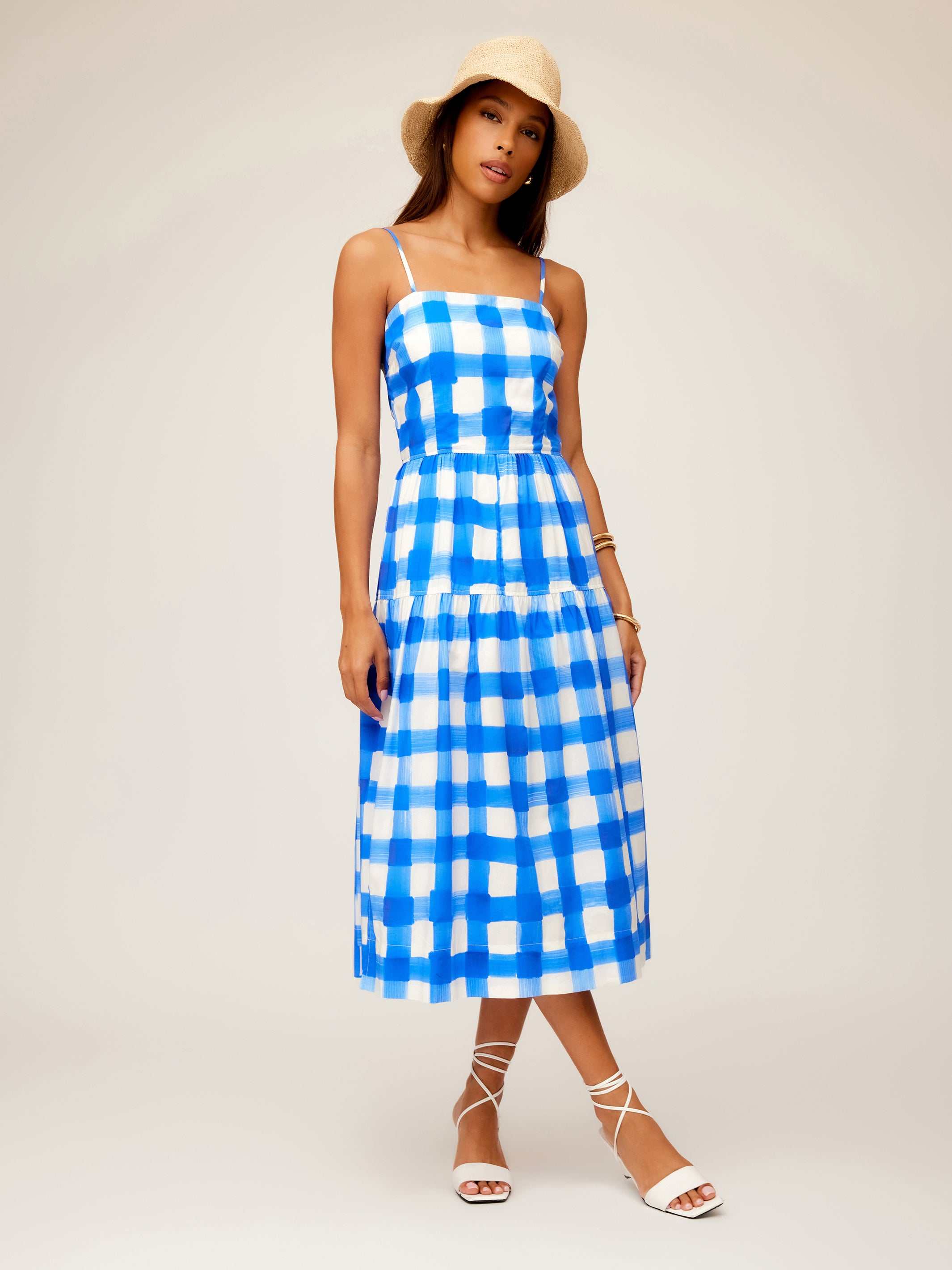 Woman wearing blue and white Costa Dress with adjustable spaghetti straps and square neck, styled with a beige hat and white sandals