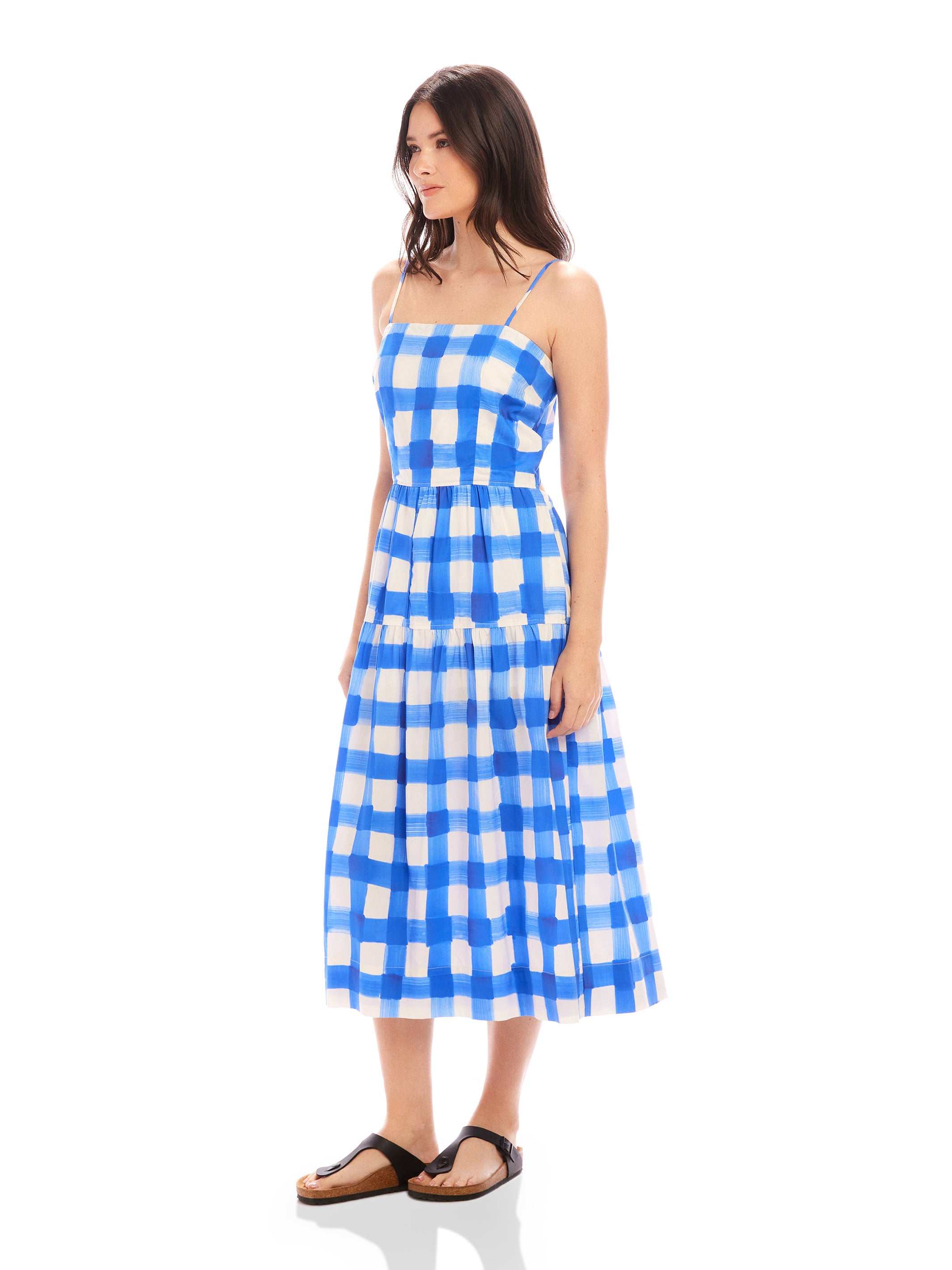 Woman wearing blue and white watercolor check Costa Dress with adjustable spaghetti straps and square neck, featuring A-line silhouette.