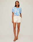 Woman wearing ecru Alma shorts with a blue patterned blouse and heels
