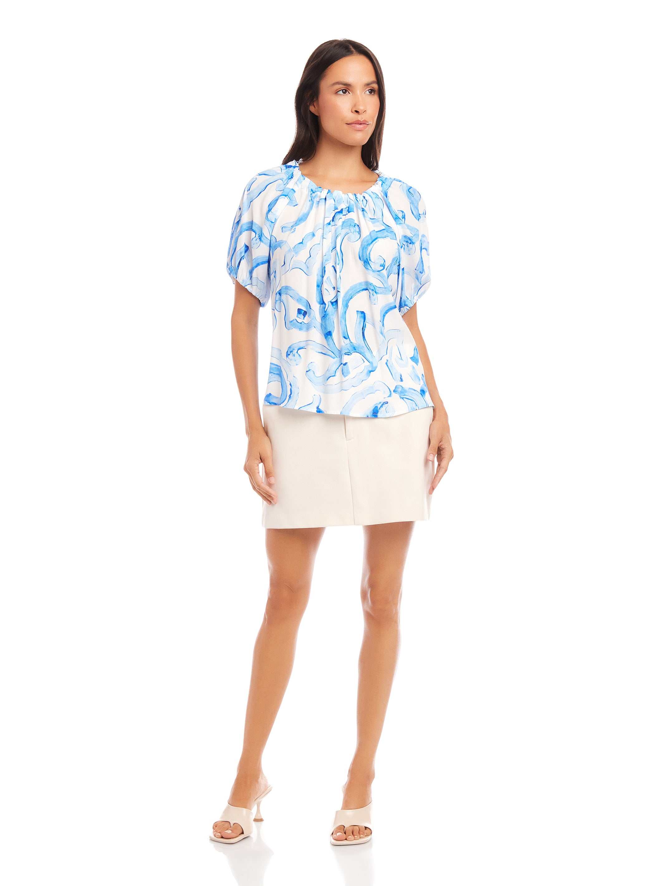 Woman wearing Savina Short Sleeve Blouse with blue painted paisley print and short puff sleeves paired with a light beige skirt