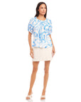 Woman wearing Savina Short Sleeve Blouse with blue painted paisley print and short puff sleeves paired with a light beige skirt