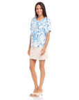 Woman wearing Savina Short Sleeve Blouse in blue painted paisley print with short puff sleeves and round neck paired with a beige skirt