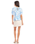 Back view of woman wearing blue painted paisley print Savina short sleeve blouse with back neck tie closure and puff sleeves