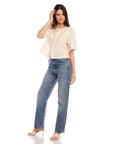 Woman wearing Nadine Bow Detail top in cream linen with front tie and short puff sleeves, paired with high-waisted blue jeans and heels