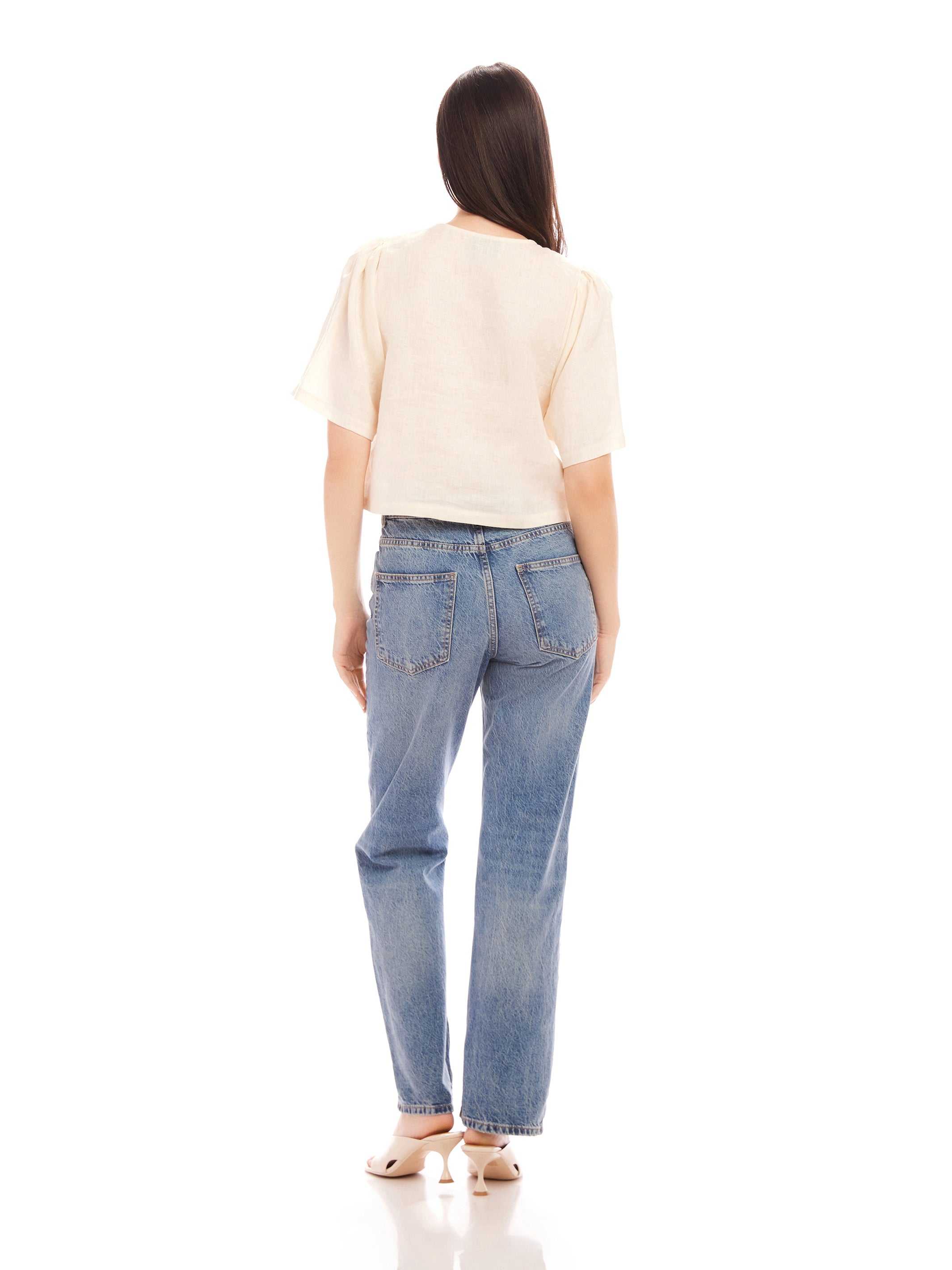 Woman wearing Nadine Bow Detail linen top with short puff sleeves and high waist jeans viewed from the back