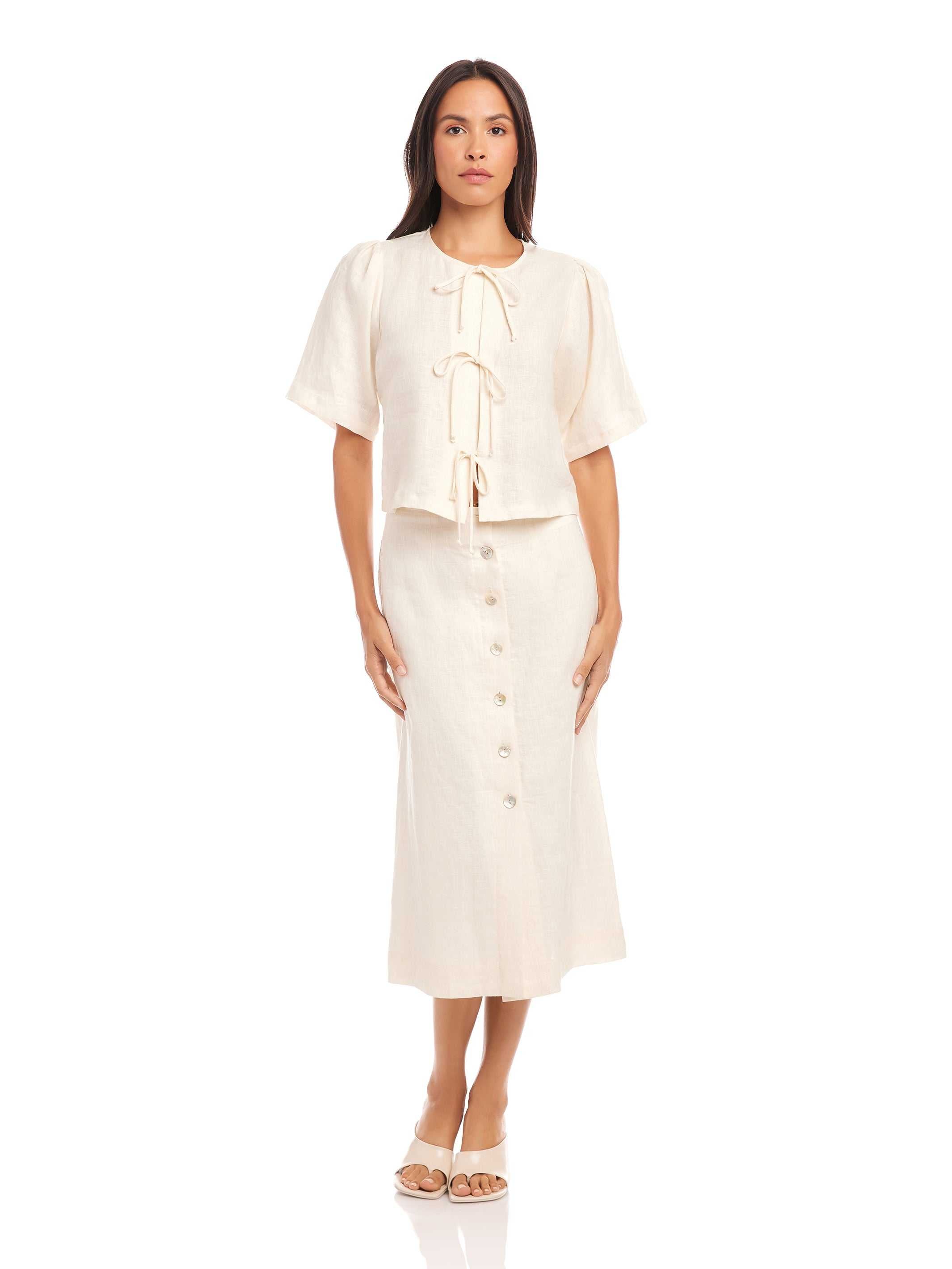 Woman wearing a cream Lori Midi Skirt with front shell buttons and a front slit made of 100% linen with straight fit and midi length