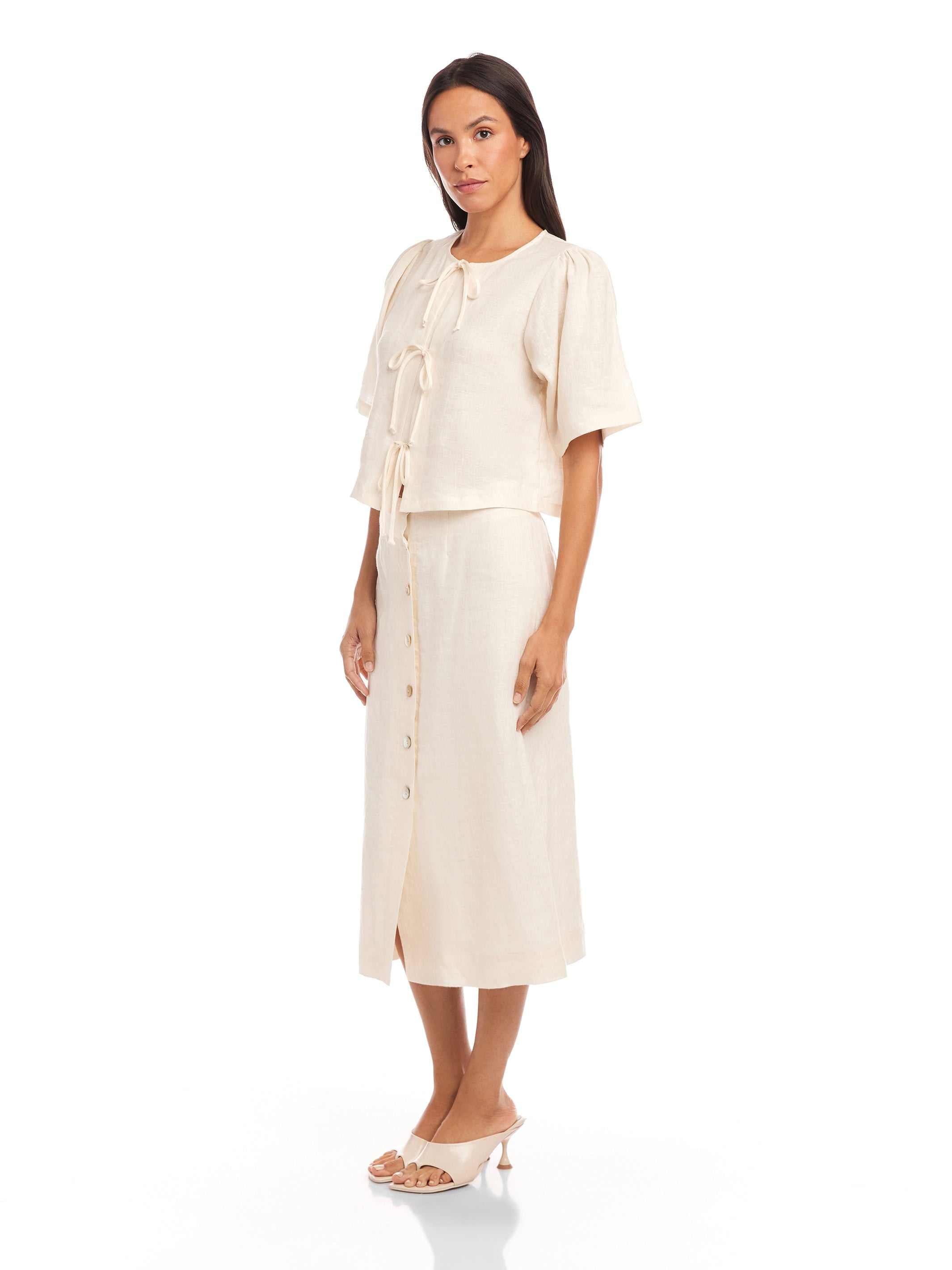Woman wearing a beige Lori Midi Skirt with front buttons and a slit, styled with a matching blouse and heels.