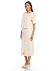 Woman wearing a beige Lori Midi Skirt with front buttons and a slit, styled with a matching blouse and heels.