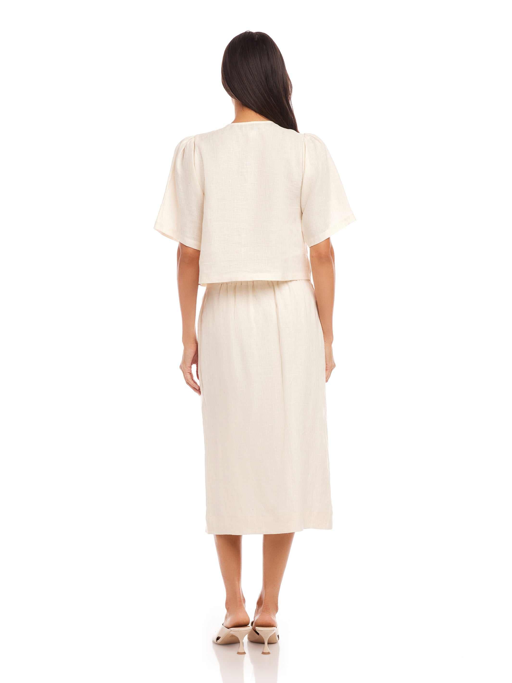 Back view of a woman wearing an off-white Lori Midi Skirt made of 100% linen with a straight fit and front slit.