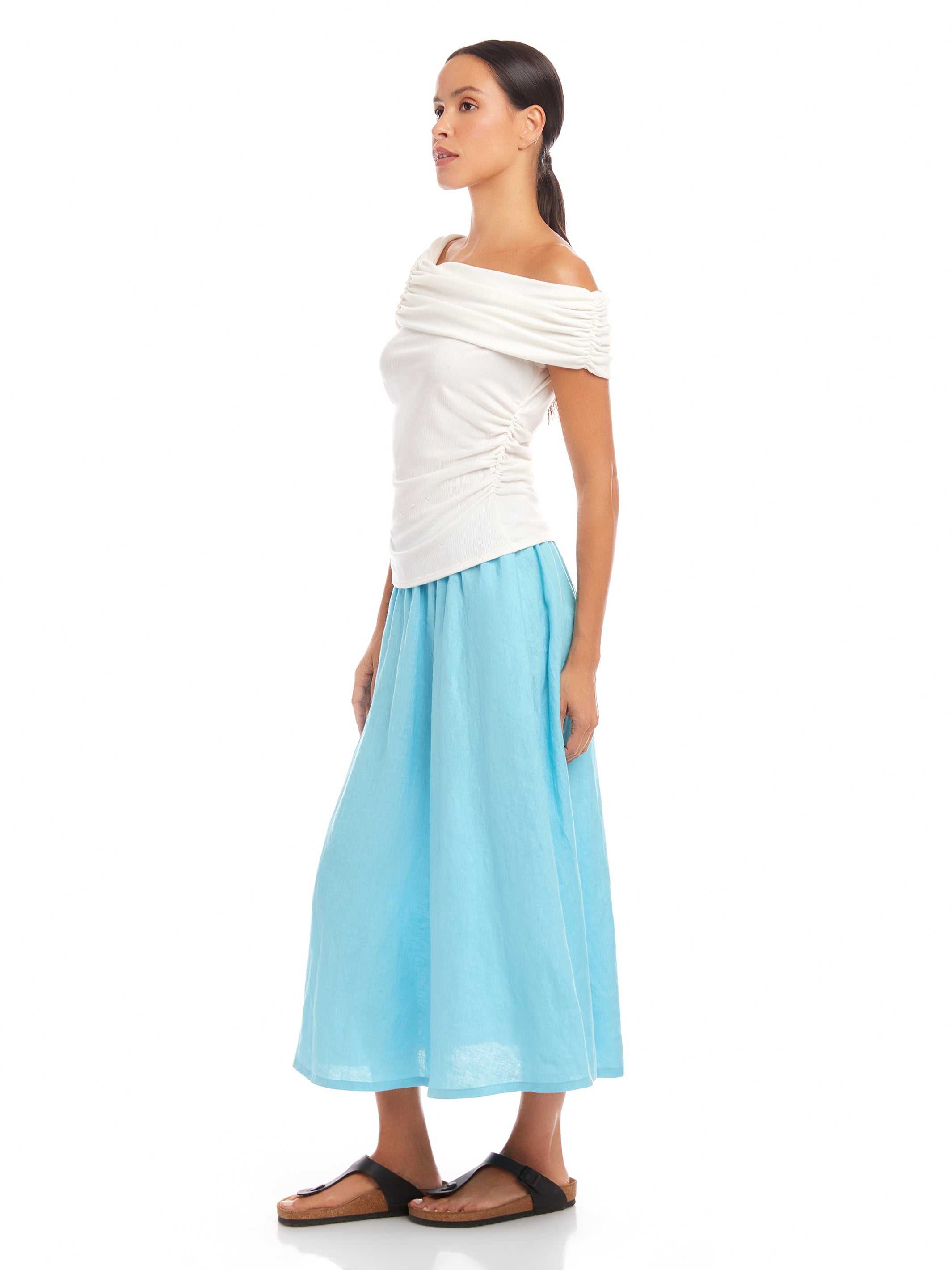 Woman wearing a white Lizzie One-Shoulder Top with asymmetrical sleeves and light blue wide-leg pants