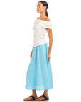 Woman wearing a white Lizzie One-Shoulder Top with asymmetrical sleeves and light blue wide-leg pants
