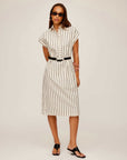 Woman wearing a collared Lucia Stripe Dress with vertical black stripes, cap sleeves, a boxy silhouette, side slit, and black belt at the waist