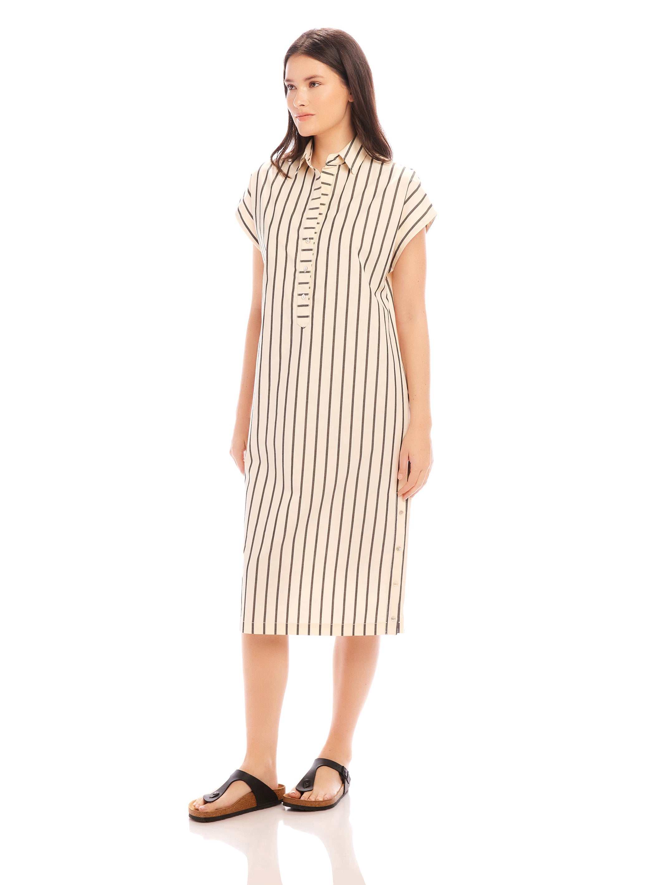 Woman wearing a sleeveless Lucia Stripe Dress with vertical stripes, collar, side slit, and buttons down the front, styled with sandals.