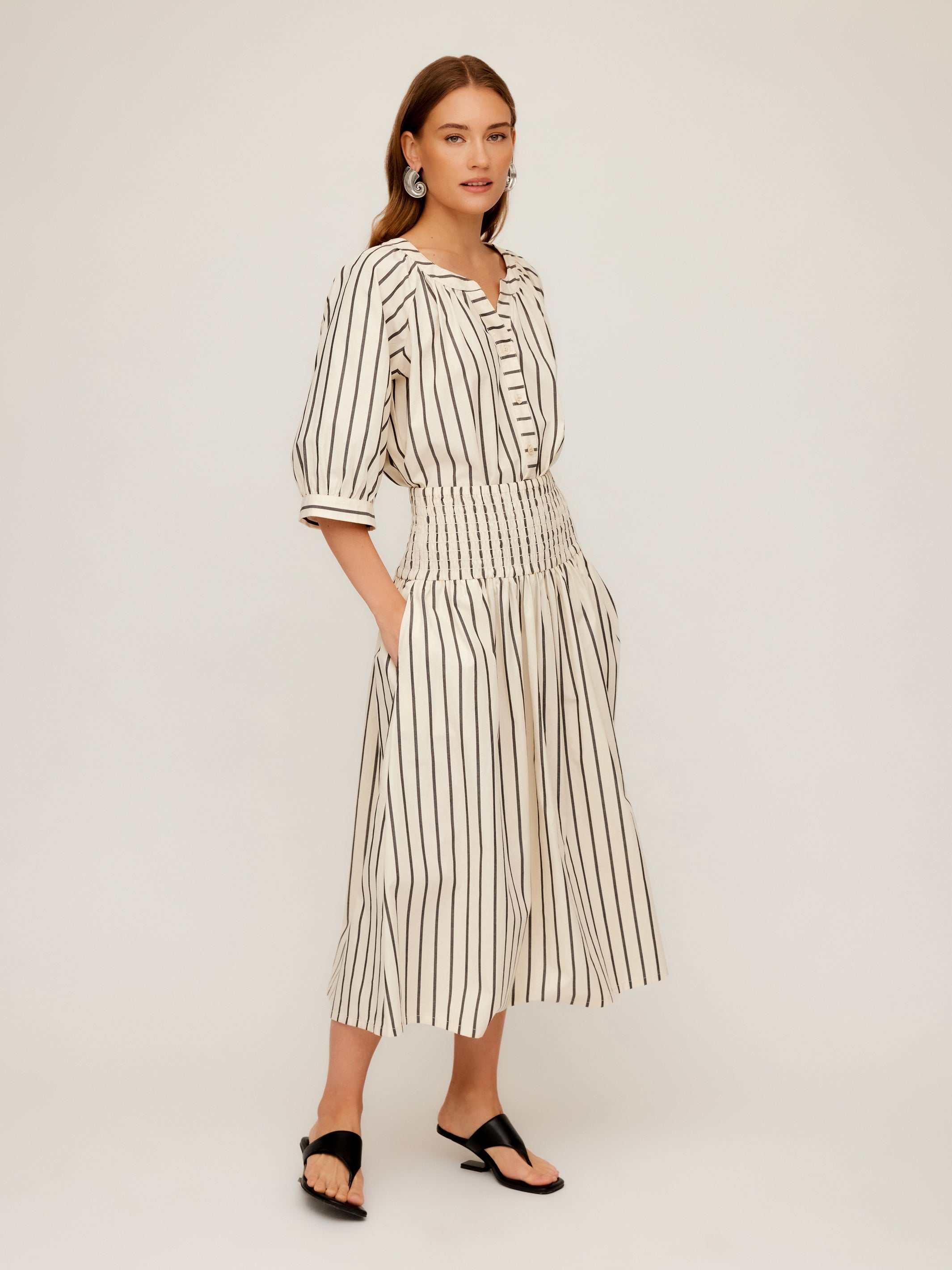 Woman wearing Rhea Stripe Skirt midi length cotton skirt with vertical stripes and elasticized sheered waist