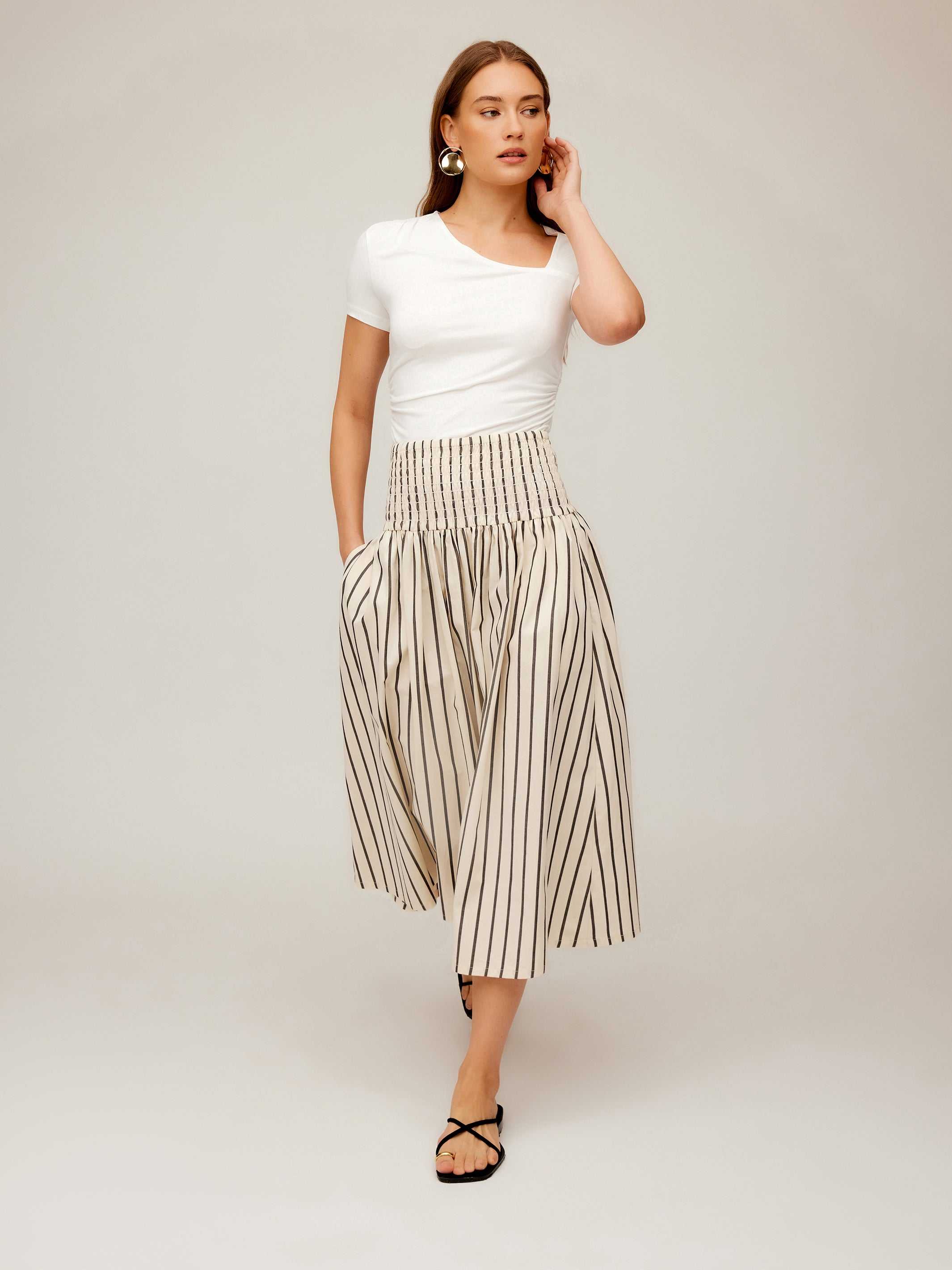 Woman wearing Rhea Stripe Skirt, a high-waisted midi cotton skirt with vertical stripes and elasticized sheered waist.